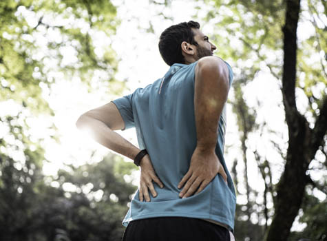 A man on a walk outside experiencing back pain.